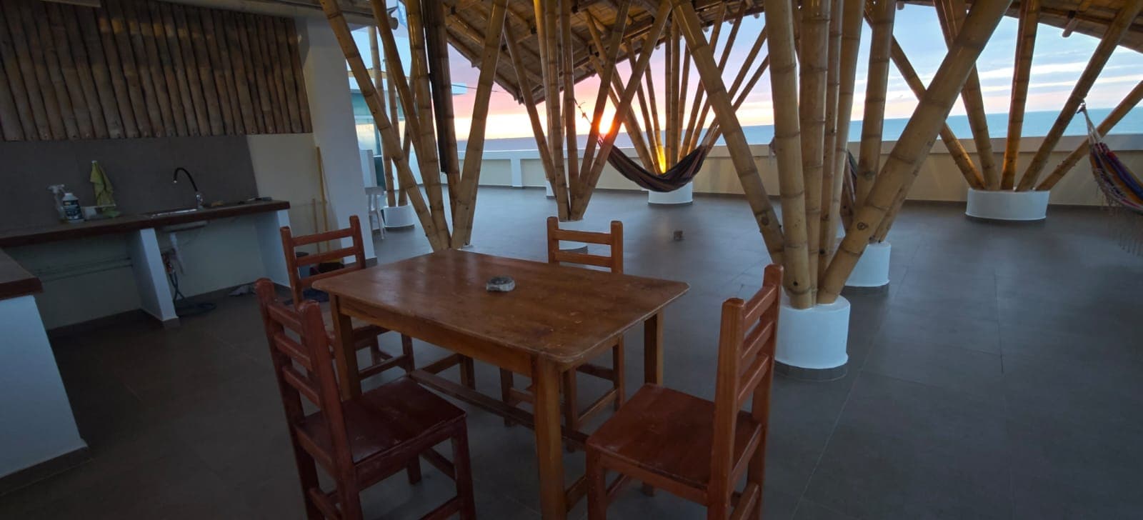Rooftop terrace with a dining table, shared kitchen and hammocks under a bamboo roof