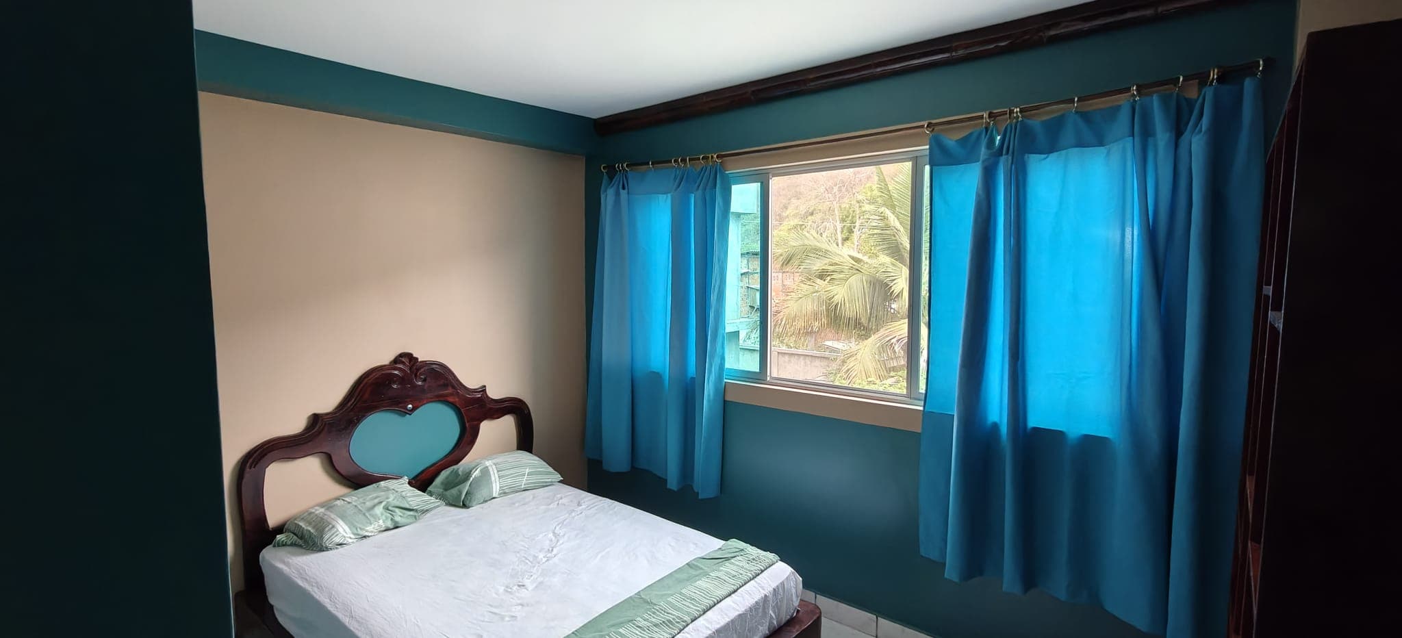 Double room with turquoise curtains and a carved wooden headboard