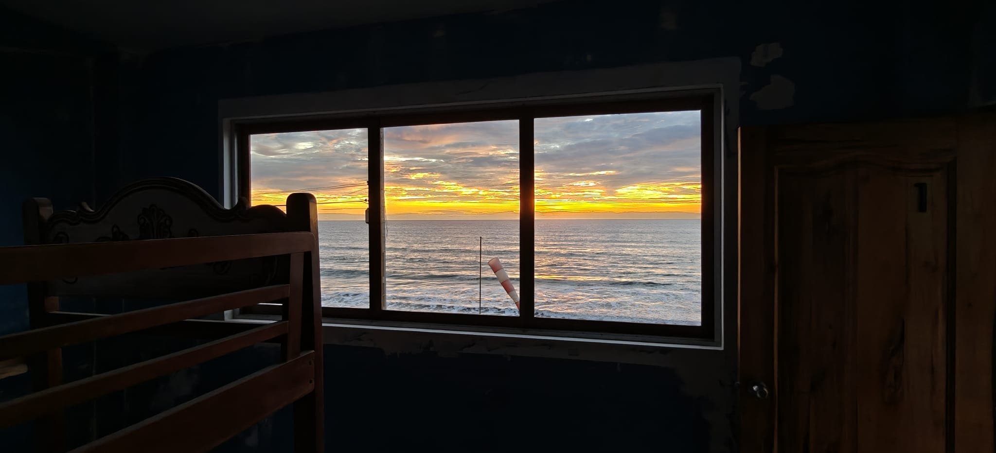 Sunset over the ocean through a room window, with a bunk bed